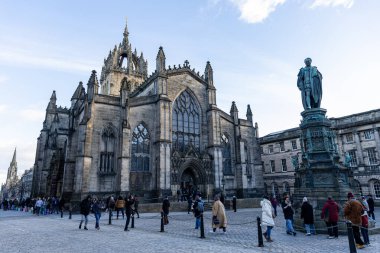 Gotik katedral ve heykel kaldırım taşı bir meydanda aydınlık bir günde Edinburgh, İskoçya 'da bulutlu bir gökyüzünün altında yürüyen insanlarla.
