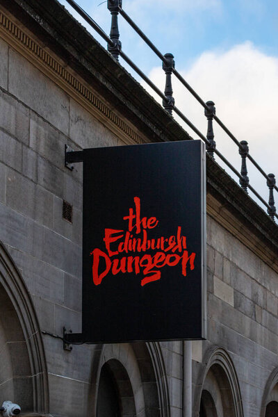 A black sign with red lettering advertising "the Edinburgh Dungeon" hangs from a stone building.