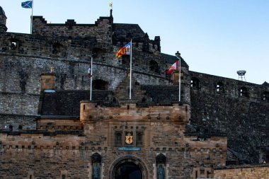 Görüntü, bayrakları dalgalanan taş bir kaleyi gösteriyor. Şatonun üzerinde bir arma ve İskoçya 'nın Edinburgh şehrinde her iki tarafında heykeller olan görkemli bir girişi var..