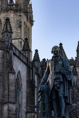 18. yüzyıldan kalma bir adamın heykeli gotik bir taş binanın önünde duruyor. Gökyüzü açık, açık mavi Edinburgh, İskoçya 'da.