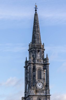 Mavi gökyüzüne karşı sivri uçlu bir kulesi olan uzun, süslü bir taş saat kulesi. Edinburgh, İskoçya 'da bir rüzgar gülüne, saate ve karmaşık mimari detaylara sahiptir..