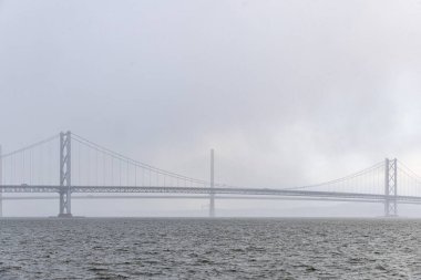Bir asma köprü ve kablo destekli köprü ağır ve bulutlu bir gökyüzünün altında bir su kütlesi boyunca paralel duruyor..
