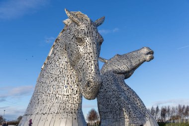 İki büyük, karmaşık şekilde inşa edilmiş paslanmaz çelik at kafası heykeli parlak mavi bir gökyüzüne karşı duruyor. Yansıtıcı yüzeyleri ve detaylı metal panelleri ışığı yakalıyor..