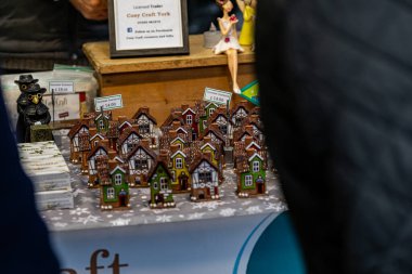 Bir tezgahta, arka planda iki veba doktoru figürü ve bir bebek bulunan bir sürü küçük renkli seramik evler sergileniyor..