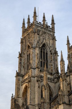 York, İngiltere 'de soluk bir gökyüzüne karşı taş oymalar, sivri kemerler ve tepelerle detaylandırılmış gotik bir katedral kulesi..