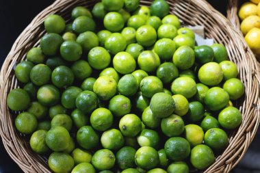 Bir markette sepete konmuş parlak yeşil limonların yakın çekimi. Doğal dokuya sahip canlı, sulu narenciye meyveleri. Tazelik, tropikal ürünler, vitamin zengini gıdalar, yemek pişirme ve organik pazarlar için idealdir..