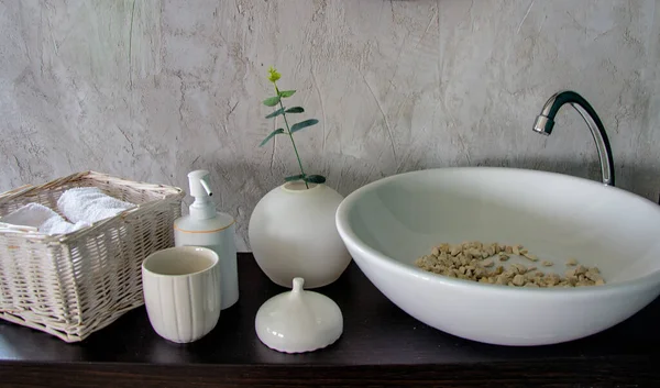 Banyo içi beyaz havlularla dolu hasır bir sepet ve içinde nehir taşları olan bir lavabo.