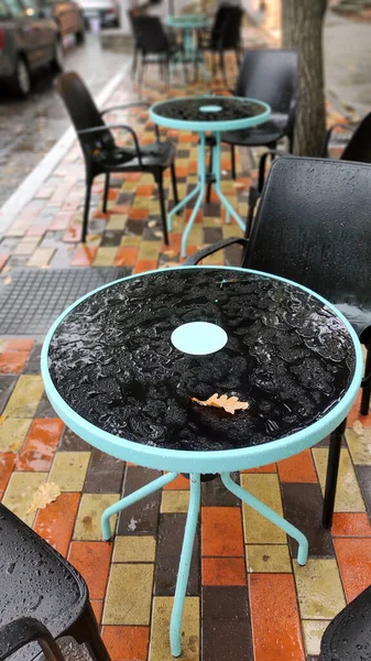 Yağmurda bir kafede boş masa ve sandalyeler.