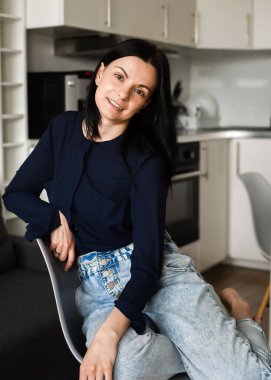 A beautiful brunette is sitting at the kitchen at home. 