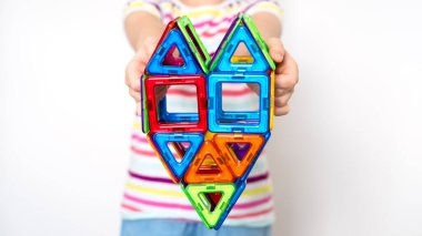 Çocuk manyetik bir oyuncakla oynuyor. Küçük bir kız çocuğu renkli bloklarla oynuyor. Kapatın. Entellektüel oyuncaklar oynayan kız. Manyetik bir yapıcıdan kalp. Pankart.