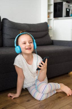 Anaokulundan bir kız evde telefonla ya da kurye ya da sosyal ağlarla iletişim kuruyor. Mavi kulaklıklı ve elinde telefon olan çocuk iletişim kuruyor..