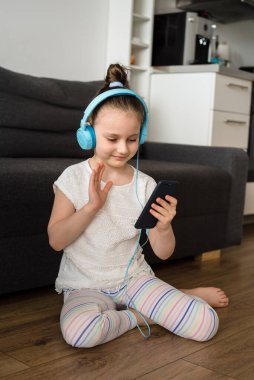 Anaokulundan bir kız evde telefonla ya da kurye ya da sosyal ağlarla iletişim kuruyor. Mavi kulaklıklı ve elinde telefon olan çocuk iletişim kuruyor..