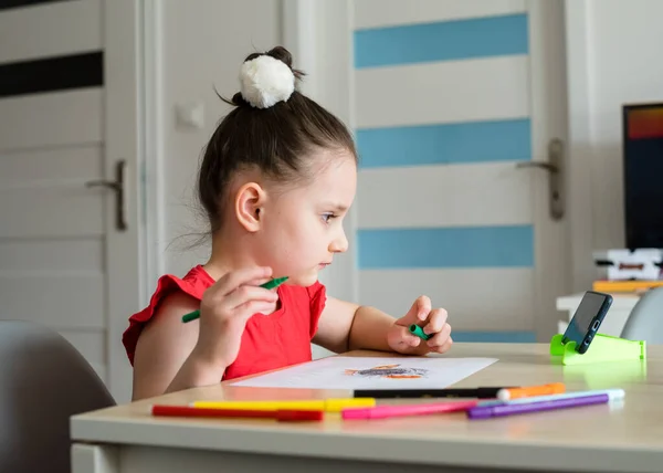 The girl draws in the kitchen from a video lesson. Home teaching, online lesson and Quarantine concept.