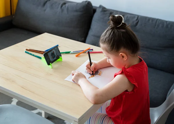 The girl draws in the kitchen from a video lesson. Home teaching, online lesson and Quarantine concept.