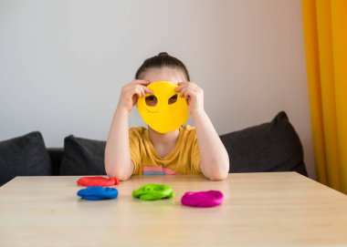 Evde sarı tişörtlü, gökkuşağı heykelleri olan bir anaokulu kızı. Çocuklar için karantina faaliyetleri.