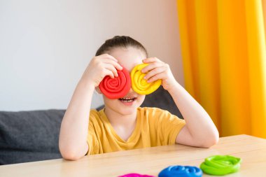 Evde sarı tişörtlü, gökkuşağı heykelleri olan bir anaokulu kızı. Çocuklar için karantina faaliyetleri.