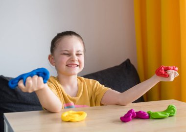 Çocuk renkli kille oynuyor. Ev yapımı plastik. Karantinadaki çocuklar için etkinlikler. İzolasyon yüzünden evde plastik heykeller yapan bir kız. Coronavirus 2021.