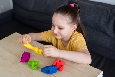 Çocuk renkli kille oynuyor. Ev yapımı plastik. Karantinadaki çocuklar için etkinlikler. İzolasyon yüzünden evde plastik heykeller yapan bir kız. Coronavirus 2021.