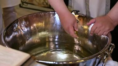 Rahip tören sırasında kutsanmış zeytinyağını vaftiz fontuna döküyor.