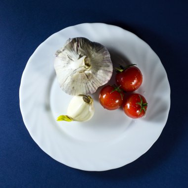 Domates ve sarımsak mavi zemin üzerine beyaz plaka