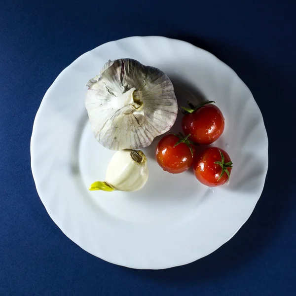 Domates ve sarımsak mavi zemin üzerine beyaz plaka