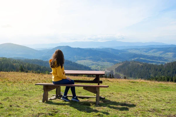 Girl sits on a wooden bench and admires the beautiful mountain landscape. Recreation. Travels. Tourism.