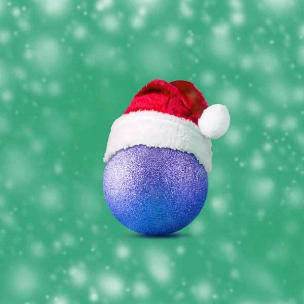 Weihnachtskugel Mit Weihnachtsmütze Auf Grünem Hintergrund Schnee Effekt Weihnachten Hintergrund — Stockfoto