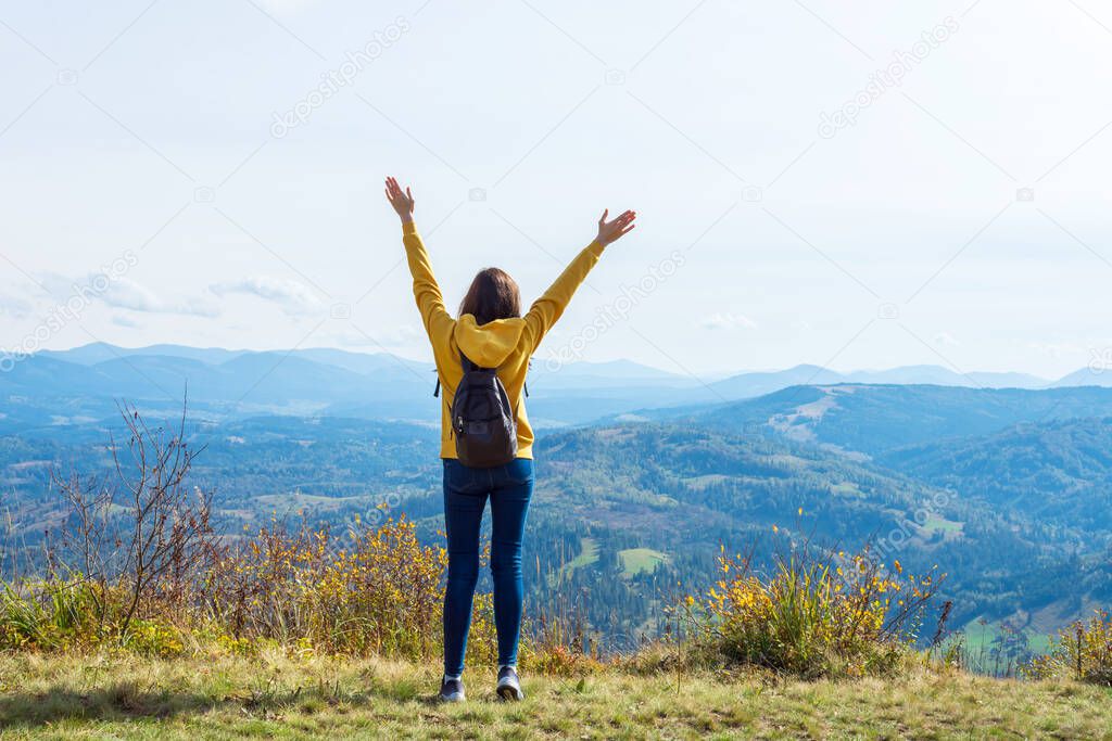 Girl in a yellow hoodie, with her hands up, on the top of a mountain. Success. Travels.