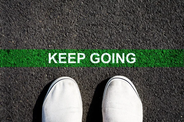 Keep Going. The inscription on the green line on the asphalt. Sneakers. View from above. Copy space. Achievement of the goal. Achieving success.