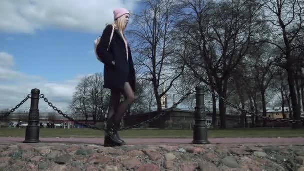 Beautiful blond teen girl walking on the sidewalk around park. She is a young — Stock Video