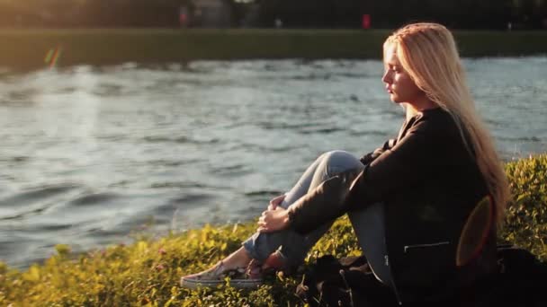 Niña descansando sobre la hierba verde cerca del río al atardecer — Vídeos de Stock