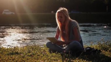 Nehri yakınında yeşil çimenlerin üzerinde oturan tablet pc ile genç kız