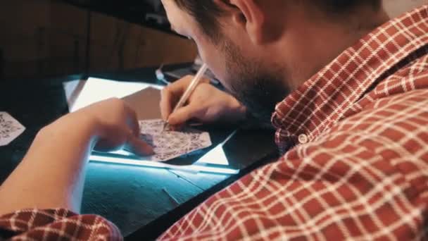 Homme barbu en chemise tressée dessine mandala motif géométrique sur une lightbox en utilisant du papier de copie — Video