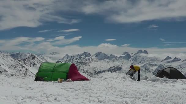 O homem ao lado da tenda turística em um fundo de picos de montanha — Vídeo de Stock