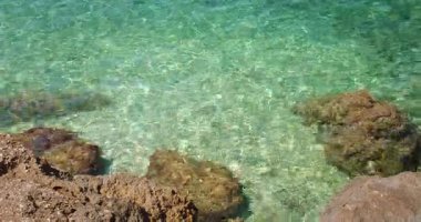 Hırvatistan 'ın Makarska kentinde güneşi yansıtan açık sığ turkuaz deniz suyuyla kayalık kıyı şeridi.