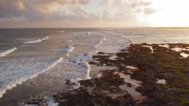 Gün batımı dalgaları kayalık kıyı şeridini gelgit havuzları ve deniz yosunlarıyla yıkıyor..