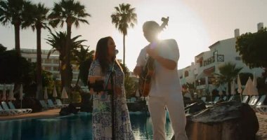 Kadın ve erkek, akşam güneşinin ışıklarıyla havuz kenarında müzik yapıyorlar..