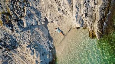 Yunanistan 'da yaz aylarında kayalıkların ve açık denizin yanında çakıllı plajda uzanan kadın.