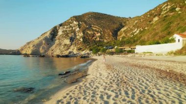 Kefalonia 'daki kayalık tepelerle Petani Sahili kıyısında yürüyen kadın.