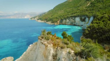 Zengin kayalıkları ve Yunanistan 'da demirlemiş teknesi olan turkuaz bir körfezde yürüyüş yapan bir kadın..