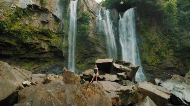 Kosta Rika 'da macera gezisi sırasında Nauyaca Şelaleleri yakınlarında kayaların üzerinde duran mutlu kadın..