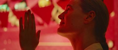 Bir kadın lüks bir dükkanın penceresinden elini kaldırarak bakarken sıcak bir şekilde gülümsüyor..