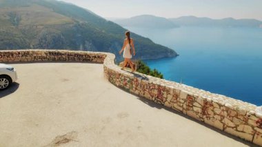 Güneşli bir yaz gününde Kefalonia 'da Myrtos Sahili manzaralı bir duvarda dengede duran bir kadın..
