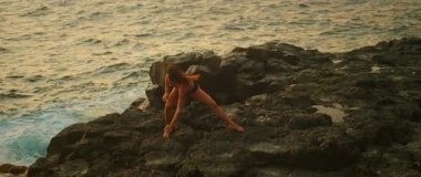 Günbatımında çağdaş dansçı kıyı kayalıklarında ilerler..