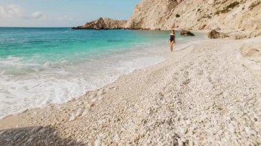 Kefalonia 'da güneşli bir günde Turkuaz Denizi kıyısında çakıl taşı plajında yürüyen bir kadın..