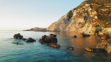 Kefalonia adasındaki bir uçurumun kenarında gün batımında kaya oluşumları sığ sulara dağıldı.