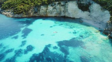 Kefalonya 'daki beyaz kayalıklar tarafından kristal berrak sularda yüzen teknenin hava görüntüsü.