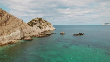 Kefalonia 'da mavi gökyüzünün altında turkuaz deniz suyu ve engebeli uçurumlarla Rocky Körfezi.