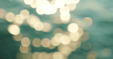 Parıldayan güneş yansımaları, okyanus dalgalanmalarında soyut bokeh desenleri yaratır..