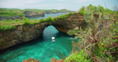 Nusa Penida Bali 'deki yemyeşil kayalıkların altında doğal taş kemer köprüsü kırılmış plaj ve turkuaz su..